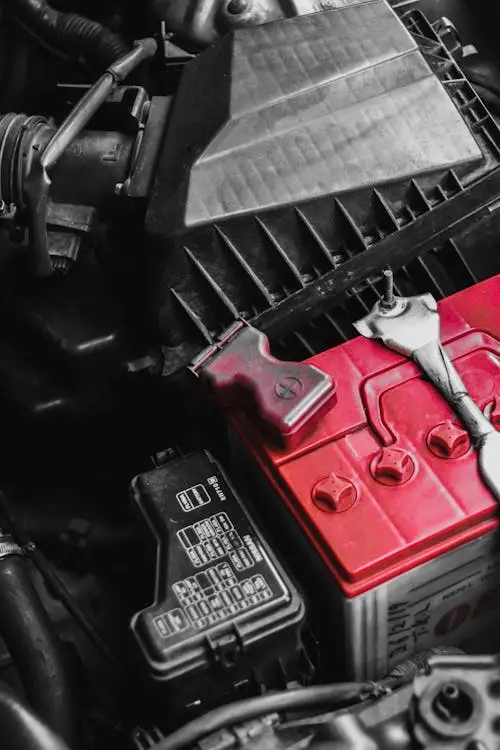 A close-up of a vehicle dashboard showing an illuminated red battery warning light symbol and dim headlights.