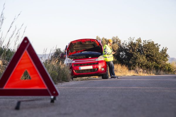 Man with relaxed attitude stranded on the road next to the broken down car talking on the phone