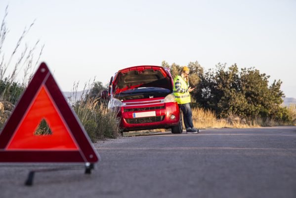 Man with relaxed attitude stranded on the road next to the broken down car talking on the phone