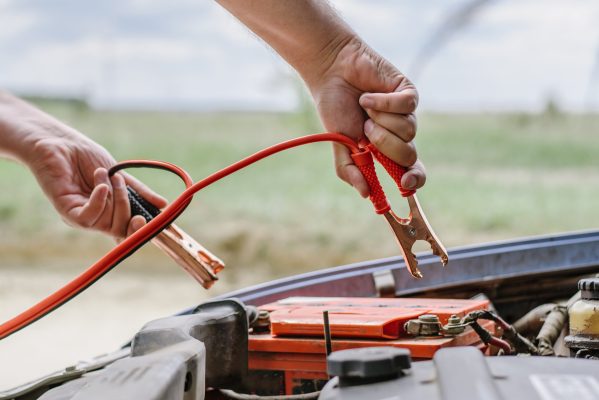 Driver using jumper cables to restart a flat car battery safely