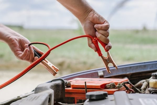 Driver using jumper cables to restart a flat car battery safely